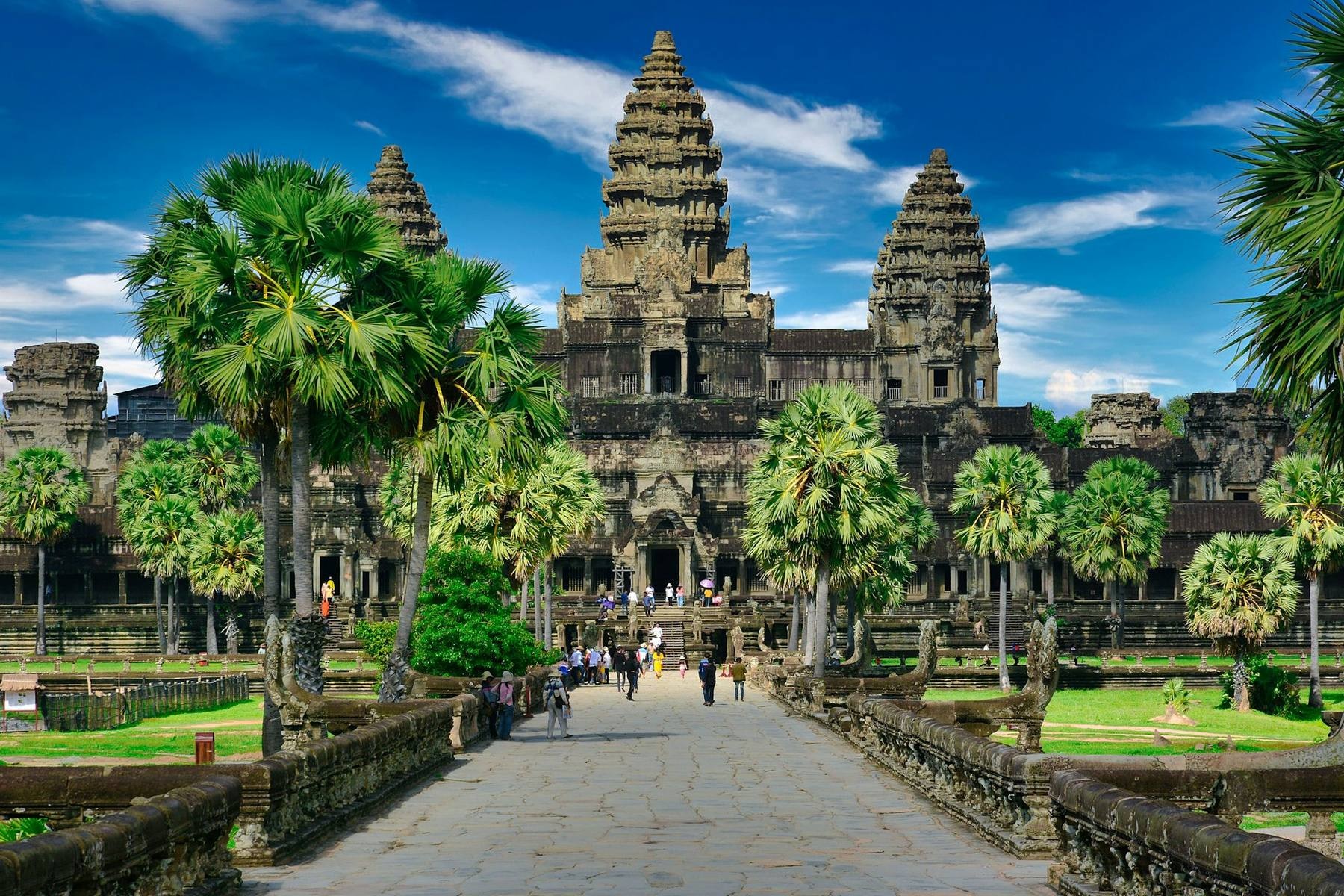 The five sandstone towers of Angkor Wat reflected in the lily pond at sunrise with monks crossing the causeway