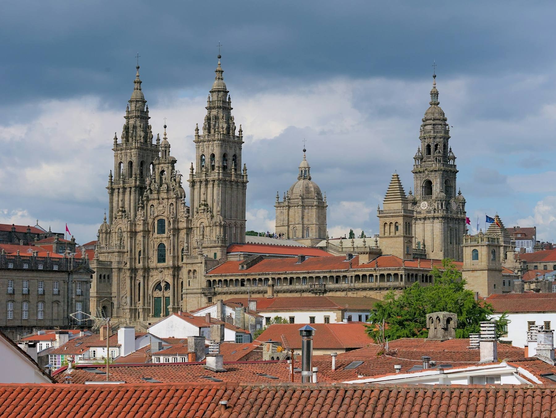 Pilgrims walking toward the Cathedral of Santiago de Compostela at dawn, scallop-shell waymarker in the foreground along the Camino Francés
