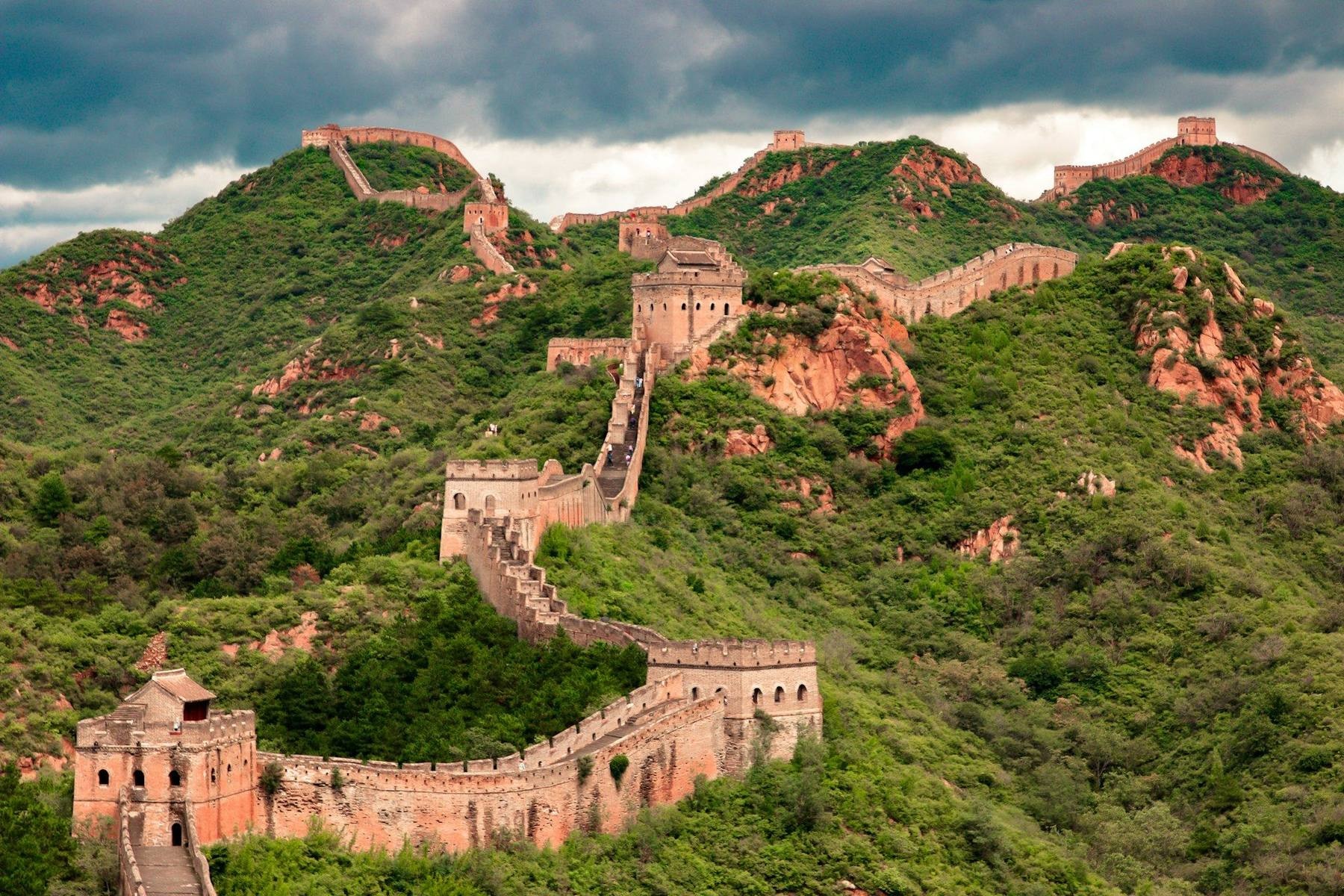 The stone ramparts of the Great Wall winding over green ridgelines into the haze at Mutianyu