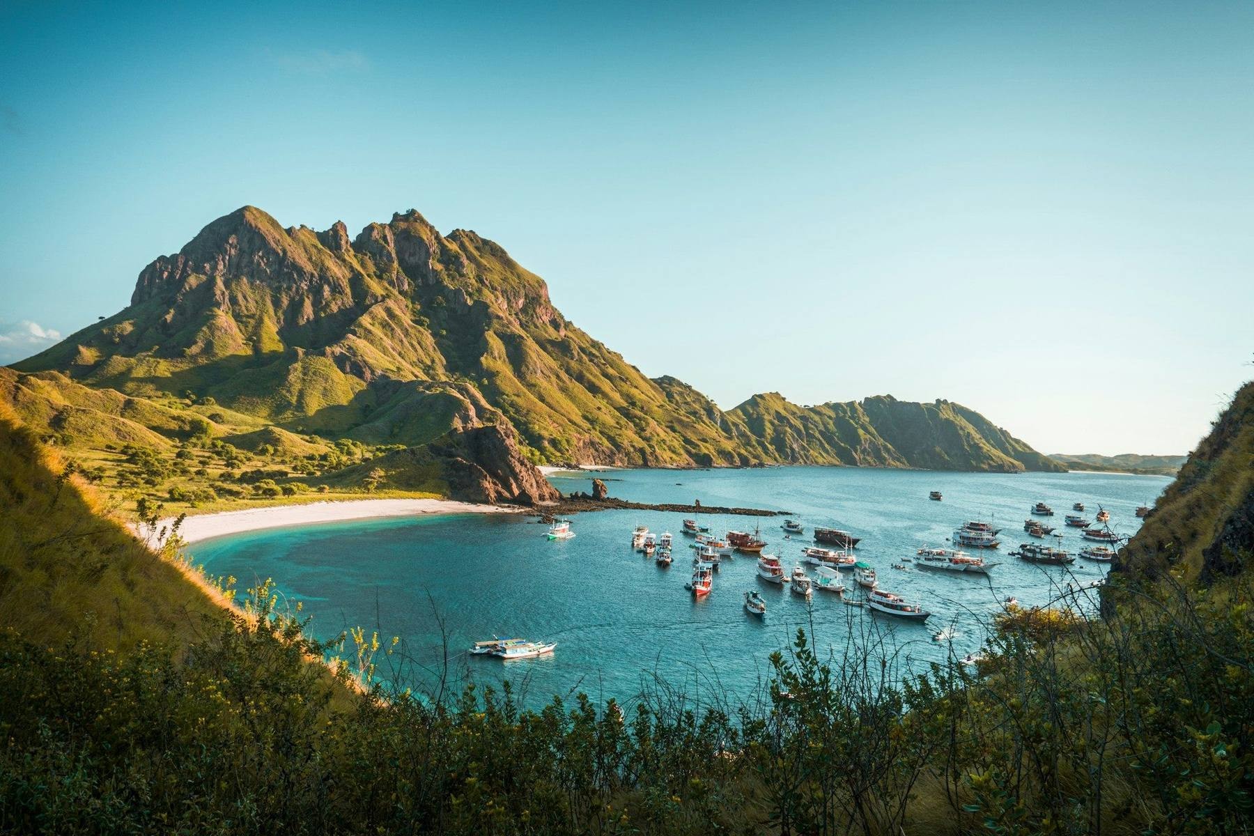 A traditional wooden phinisi liveaboard anchored off a green island in Komodo National Park with open sea beyond
