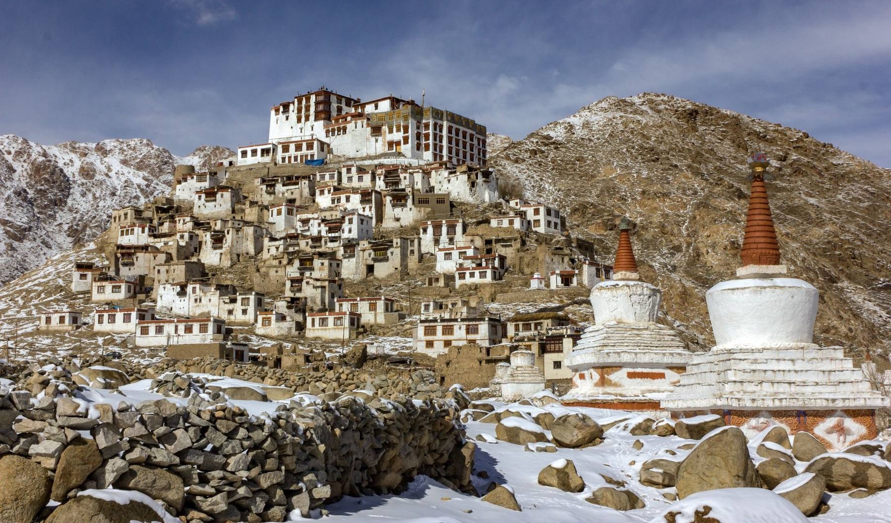 A high-altitude monastery perched on a rocky ridge in the Indus Valley with snow-capped Ladakh range peaks behind it