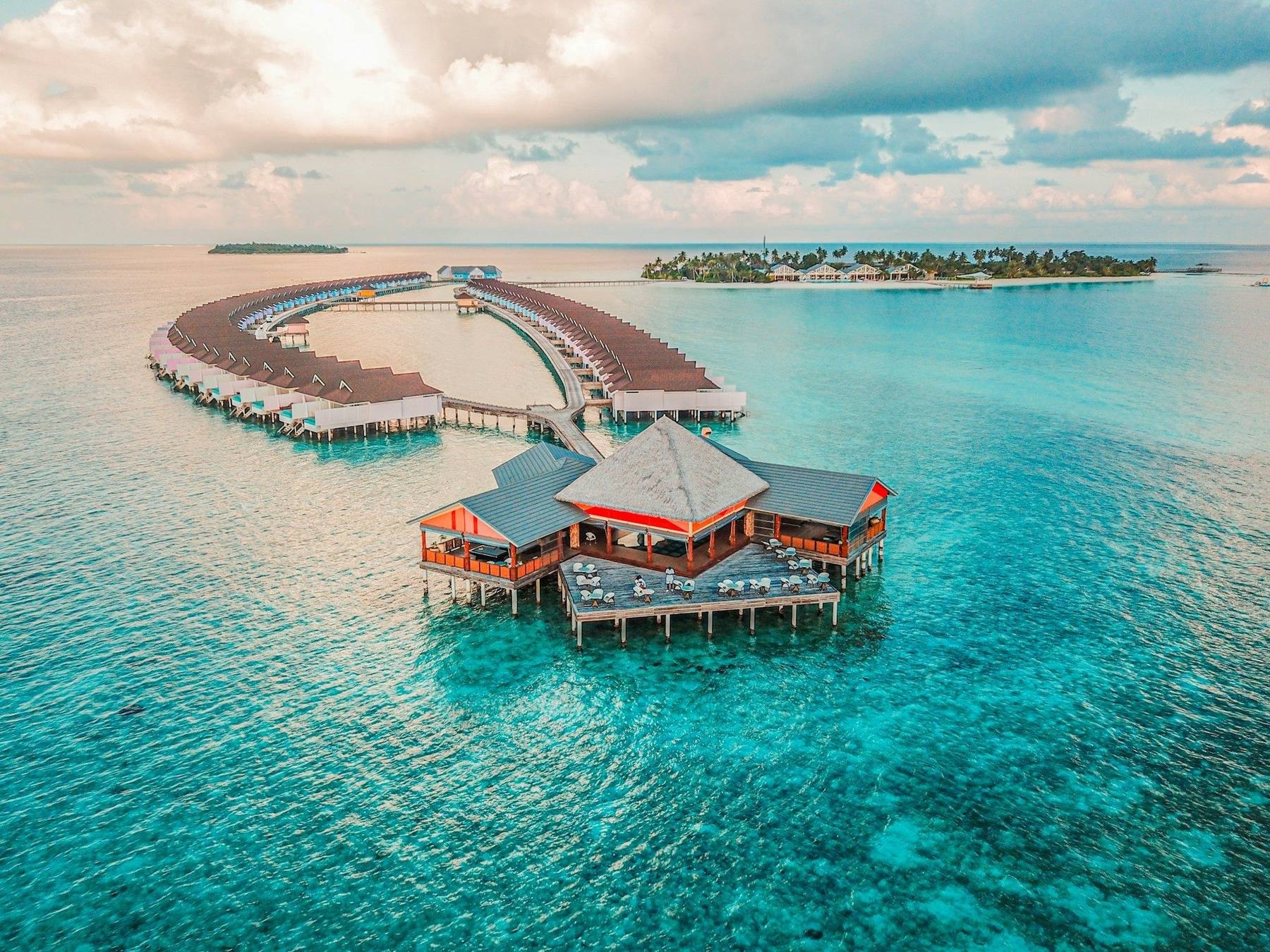 A de Havilland Twin Otter seaplane on floats taxiing past overwater villas in a turquoise Maldives atoll lagoon