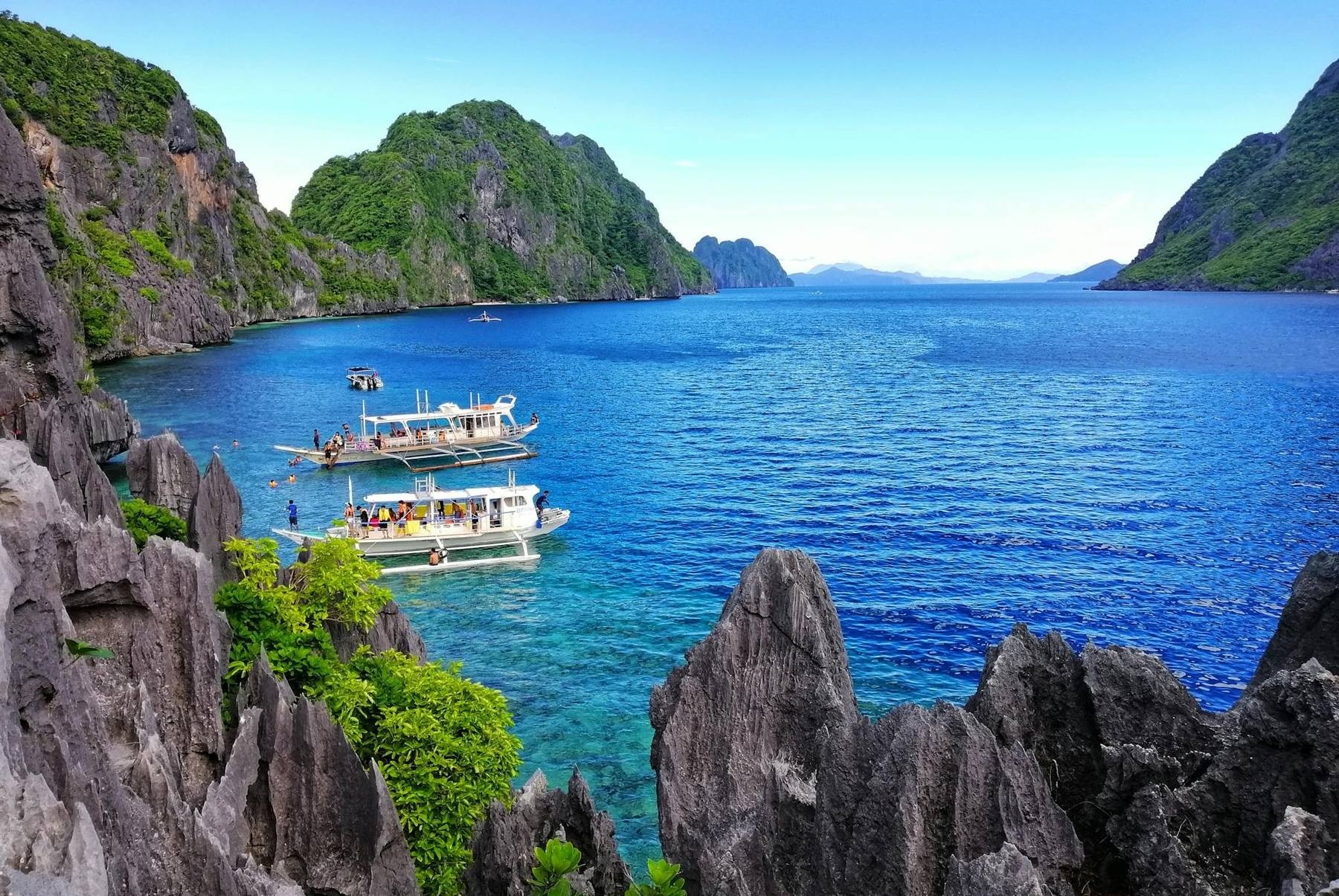 Wooden banca outrigger boat anchored in a turquoise lagoon ringed by limestone karsts in El Nido, Palawan