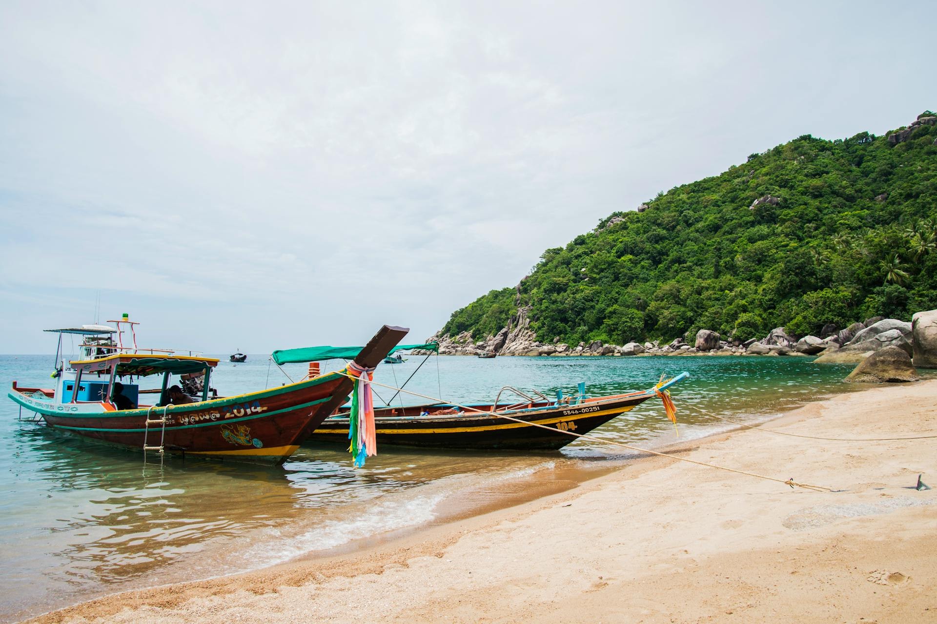 Long-tail boats moored off a limestone-cliff beach in southern Thailand at golden hour