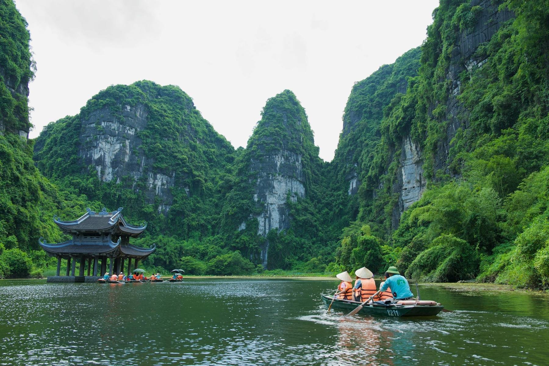 Limestone karsts of Halong Bay at golden hour with a traditional red-sailed junk in the foreground and the Hanoi-Hoi An-Ho Chi Minh travel circuit implied by an open day pack on the deck